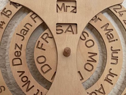 Ewiger Kalender aus präzise gelasertem Flugzeugsperrholz mit drei drehbaren Holzscheiben für Datum, Monat und Wochentag. Die Beschriftung der Ringe ist mit einem feinen Gravierstichel eingraviert und sorgt für klare, langlebige Markierungen. Das Objekt verbindet funktionales Design mit sorgfältiger Holzhandwerkskunst.